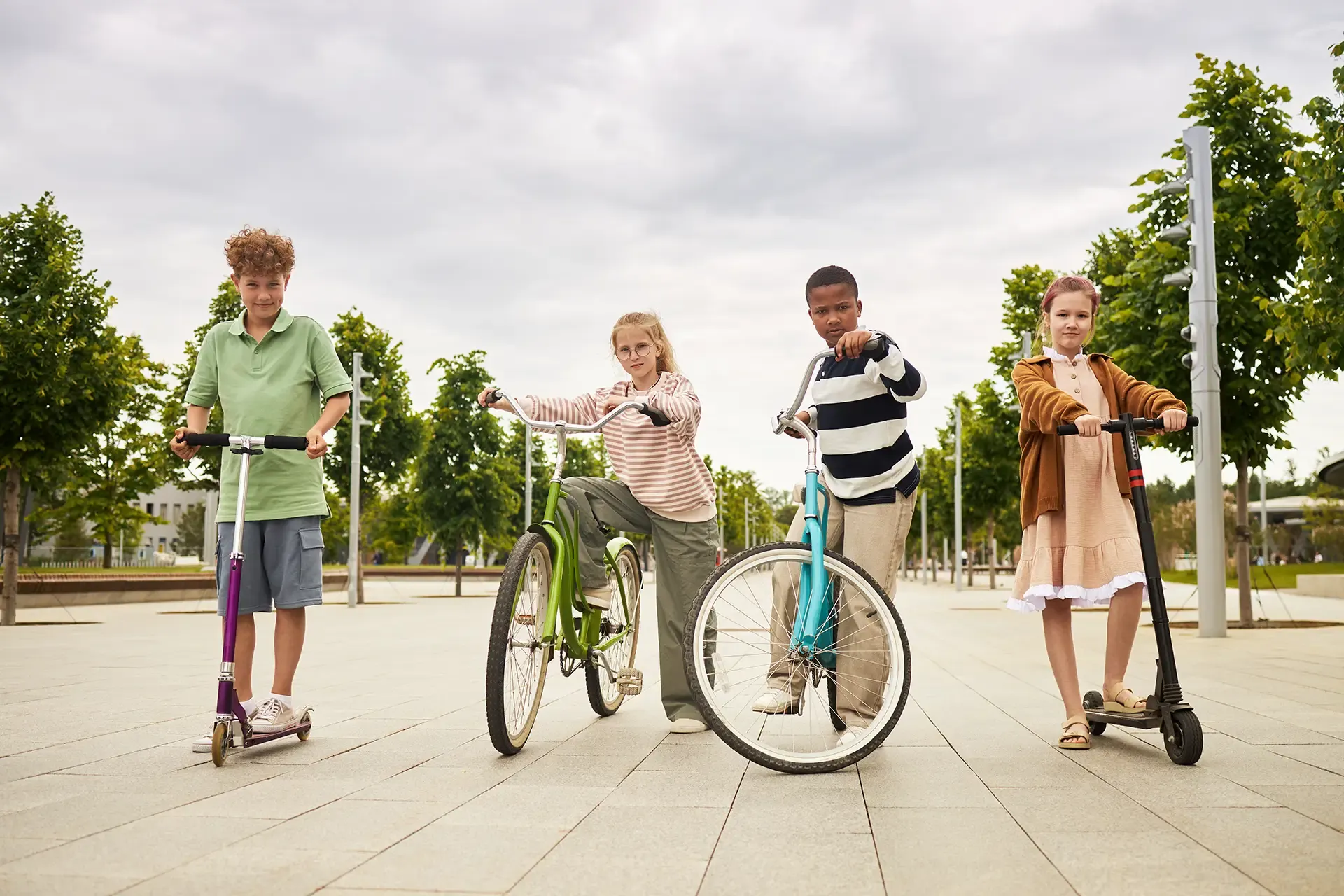 Vier Kinder mit Rollern und Fahrrädern im Park